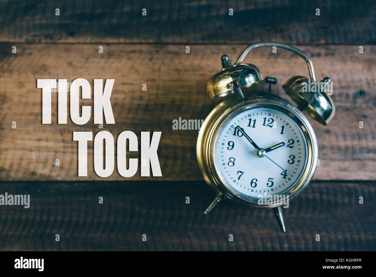 Tick tock giorno concetto - golden bell orologio su una tavola di legno sfondo con 'tick tock" parola Foto Stock