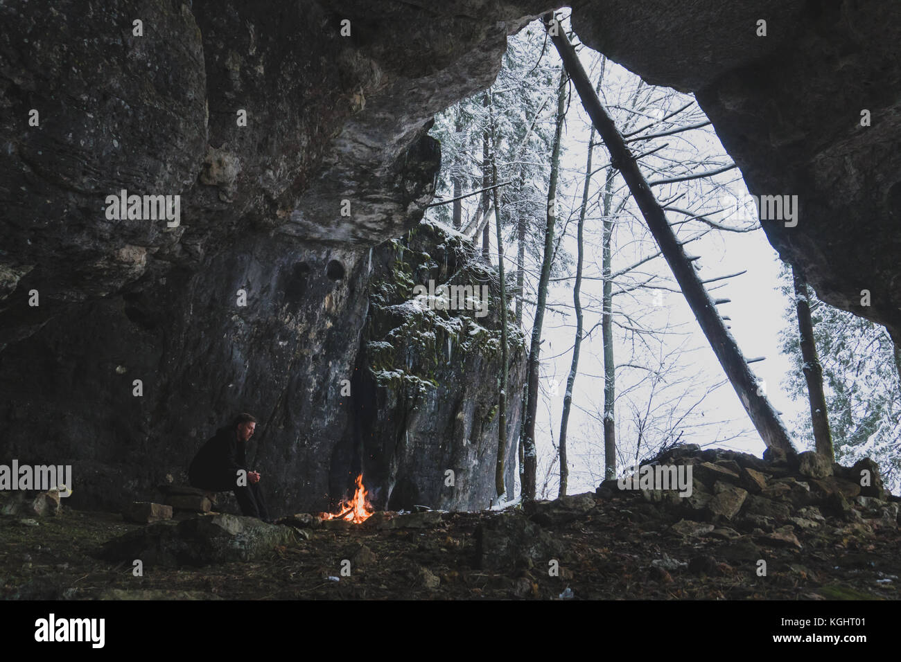 Un uomo con una barba guarda il fuoco vicino alla grotta Foto Stock