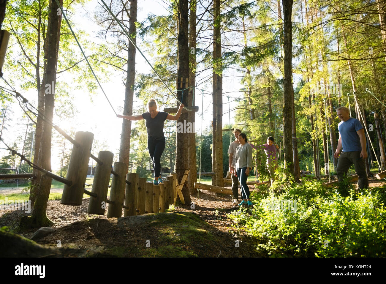 Gli amici a guardare la donna attraversando il ponte di log in foresta Foto Stock