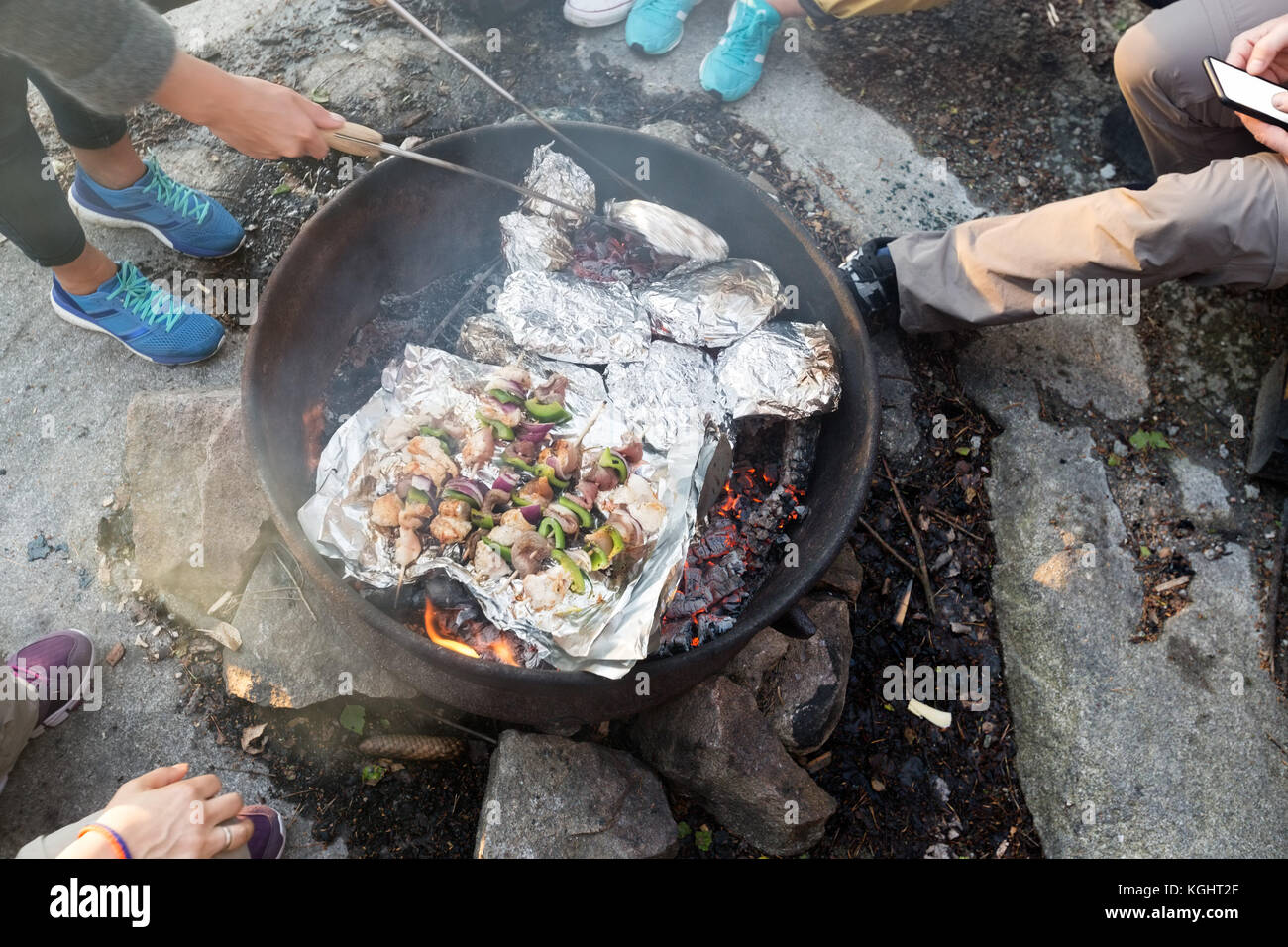Gli amici la cottura alla griglia di cibi in firepit al forest durante l escursione Foto Stock