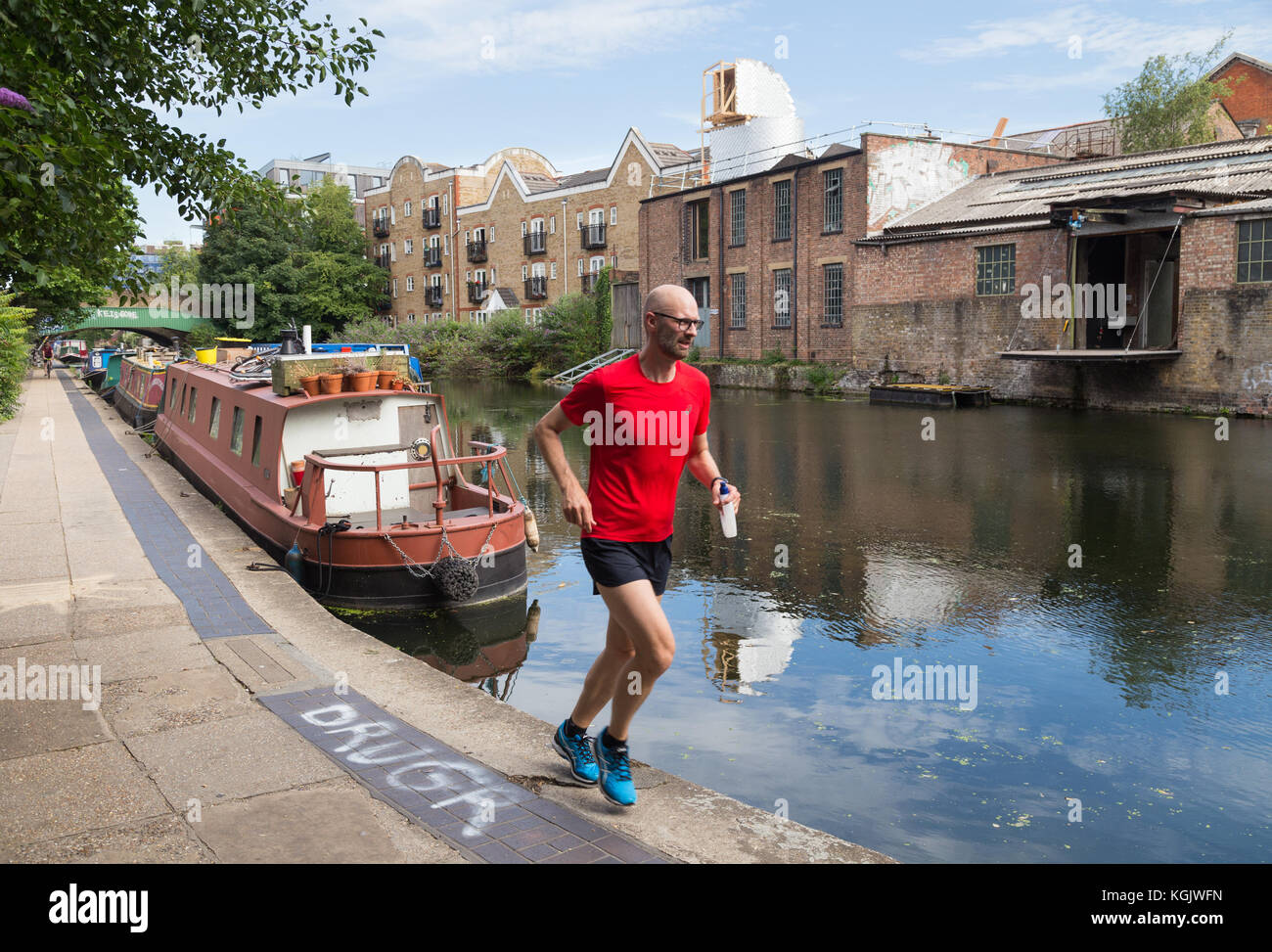 Un uomo in una T-shirt rossa fa avanzare lungo la strada alzaia dal Regent's Canal, tra il quartiere di Islington e Hackney a Londra, Regno Unito Foto Stock