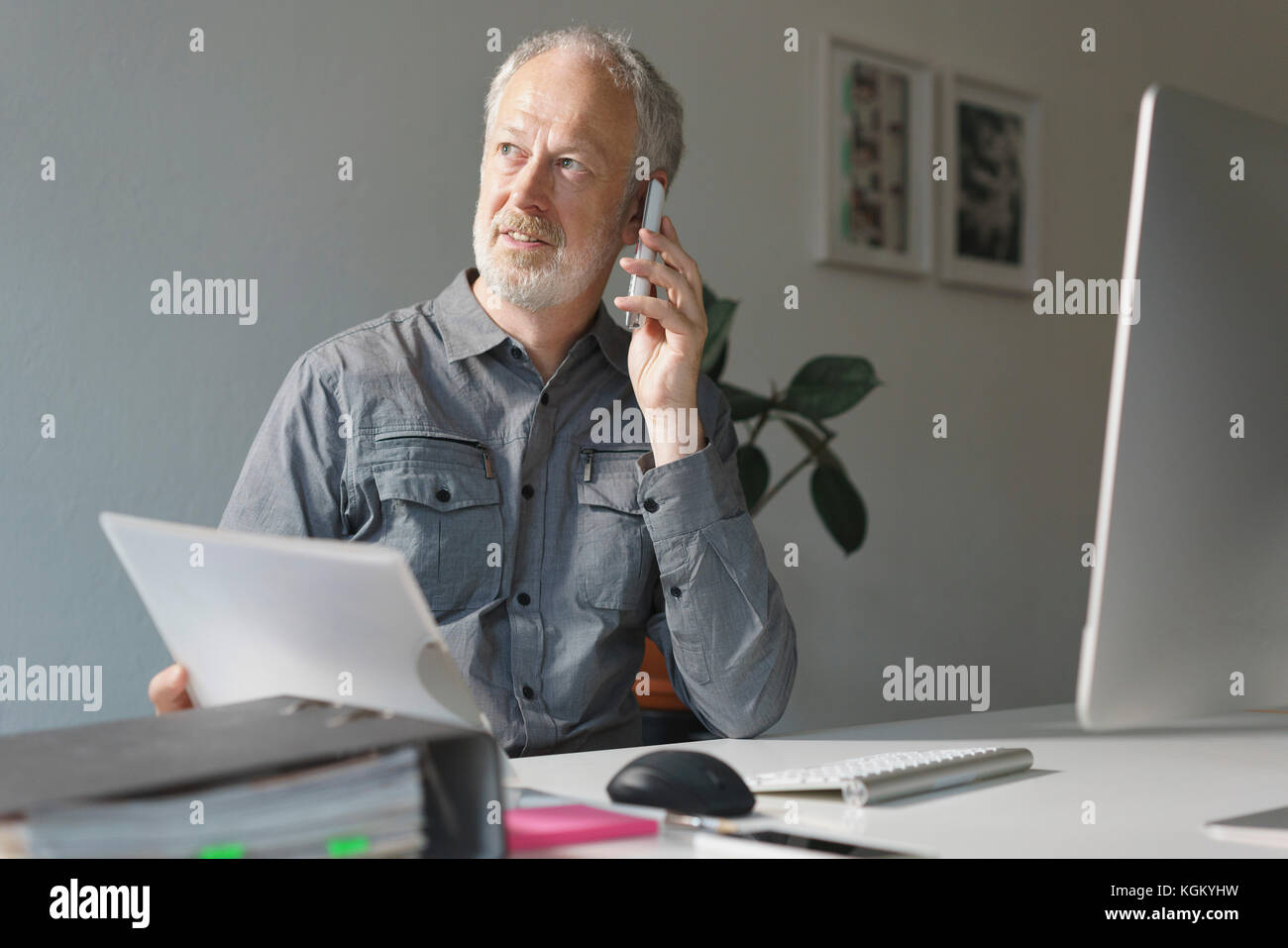 Imprenditore maturo utilizzando il telefono cellulare mentre è seduto alla scrivania in ufficio Foto Stock