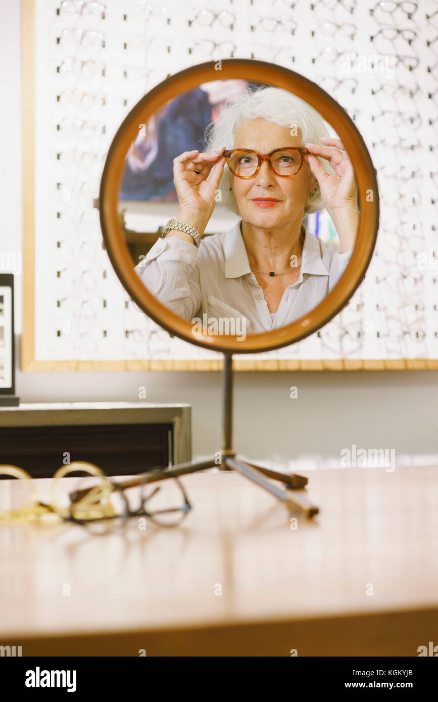 Ritratto di donna senior indossando occhiali riflettendo sullo specchio in negozio Foto Stock
