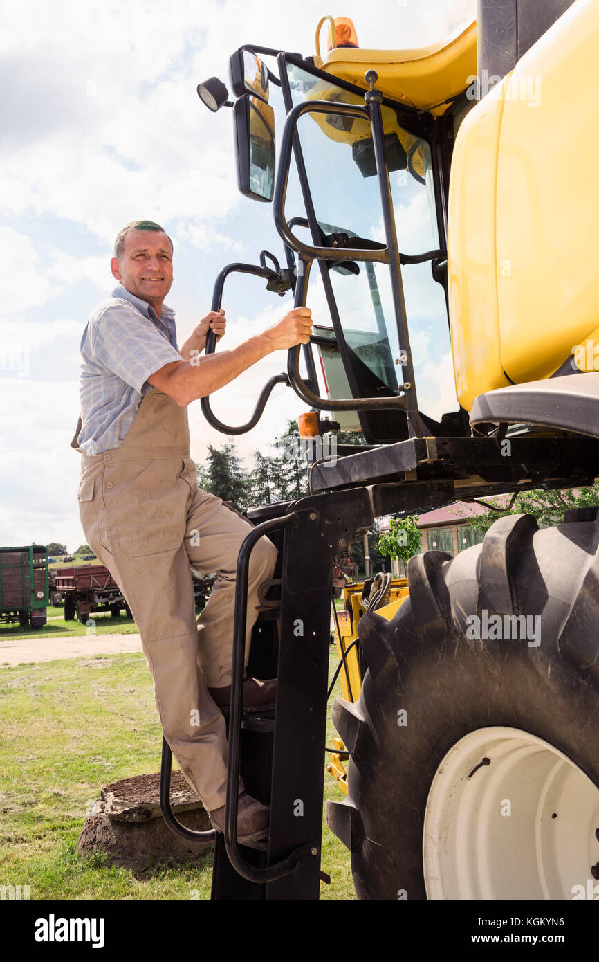 Lunghezza completa dell'uomo arrampicate sulle macchine agricole presso l'azienda contro sky Foto Stock