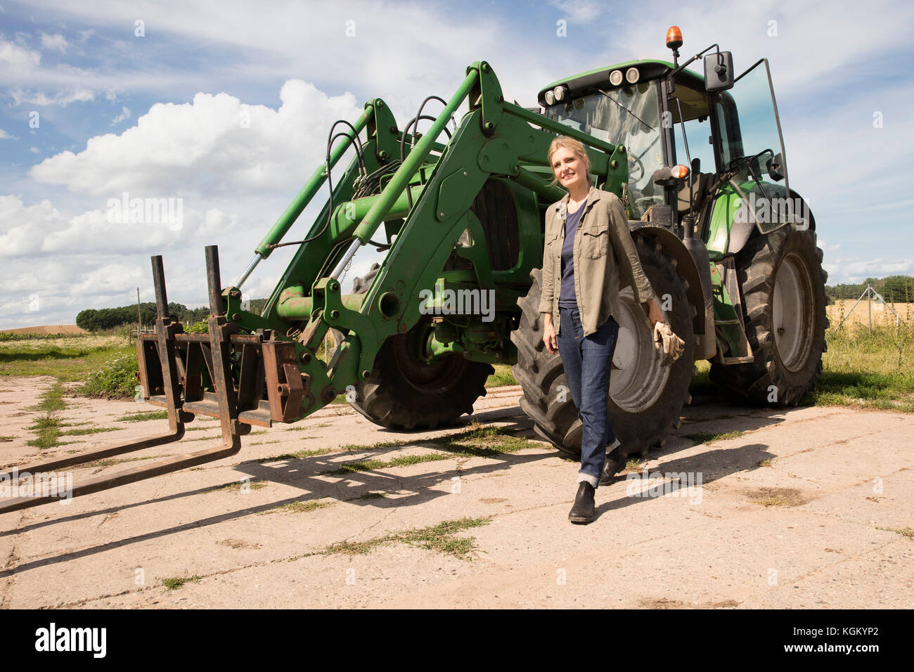 Sorridente donna matura a piedi da macchine agricole presso l'azienda contro sky Foto Stock