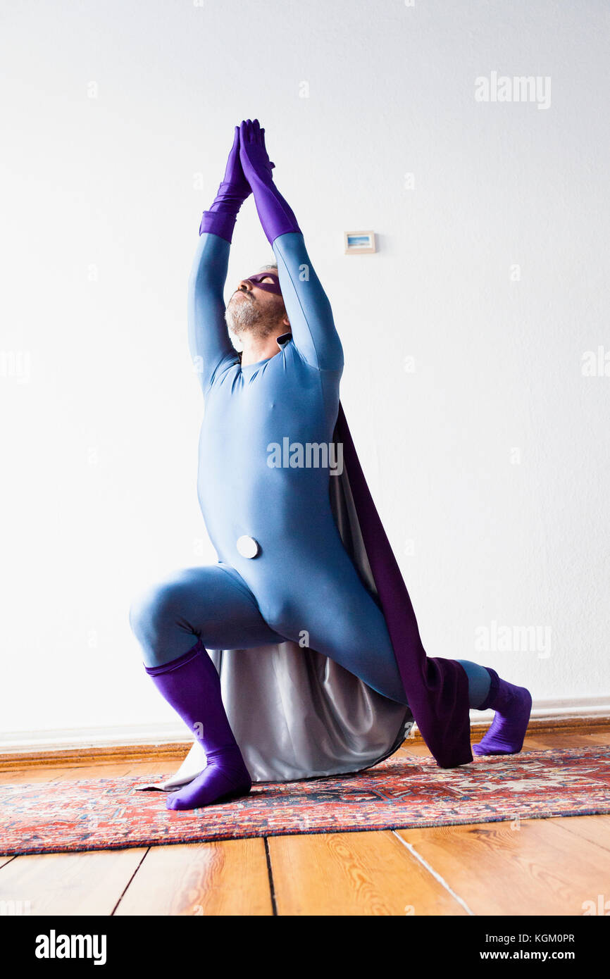 Il supereroe che la pratica dello yoga sul tappeto contro il muro bianco Foto Stock