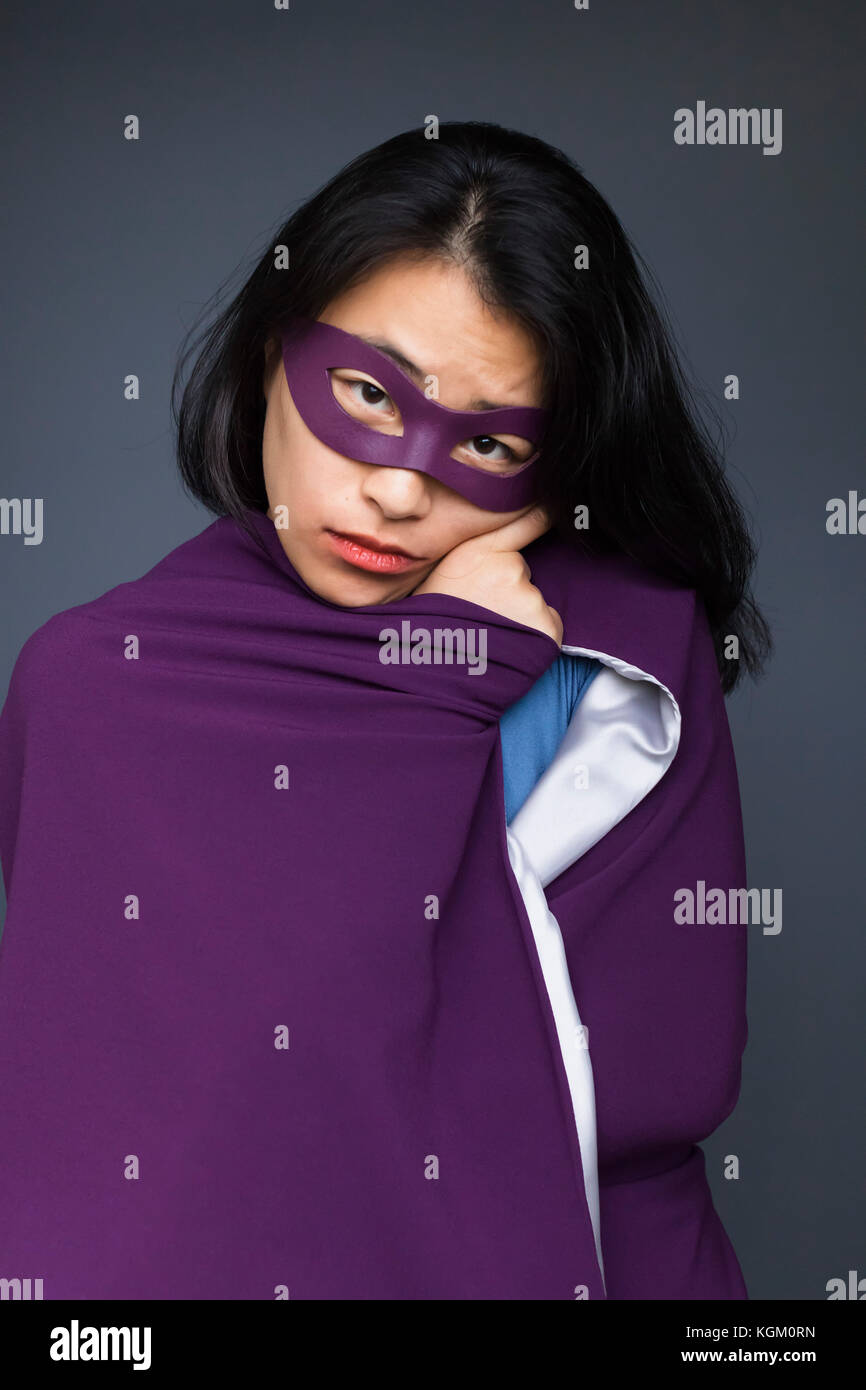 Ritratto di supereroe femminile viola che indossa il capo in piedi contro lo sfondo grigio Foto Stock
