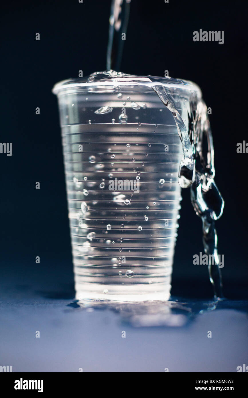 Close-up di acqua versando in un impeto di vetro sul tavolo su sfondo nero Foto Stock