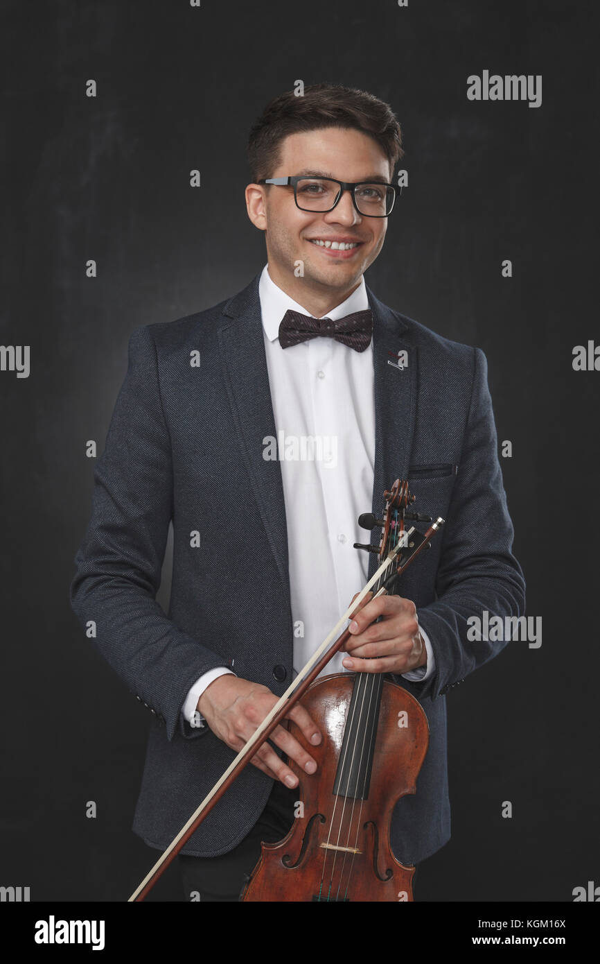 Ritratto di sorridente giovane azienda violino mentre in piedi su sfondo nero Foto Stock