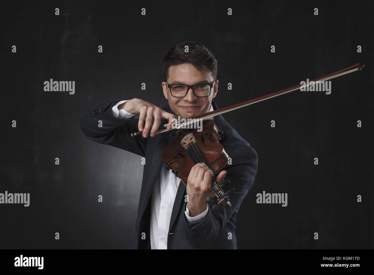 Fiducioso sorridente giovane uomo suona il violino mentre in piedi su sfondo nero Foto Stock