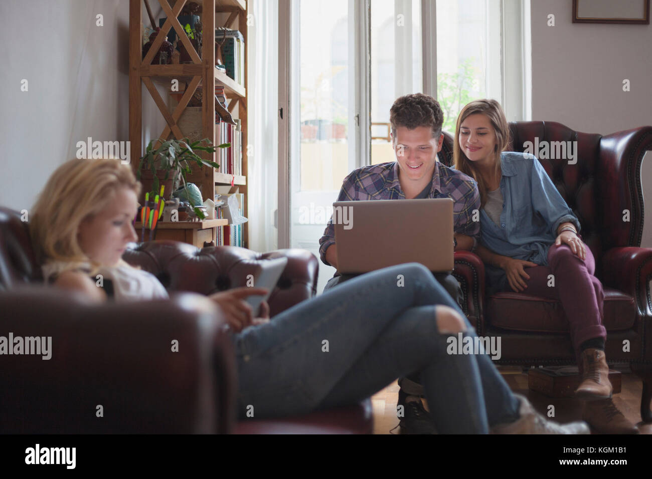Donna con tavoletta digitale mentre gli amici utilizzando portatile a casa Foto Stock
