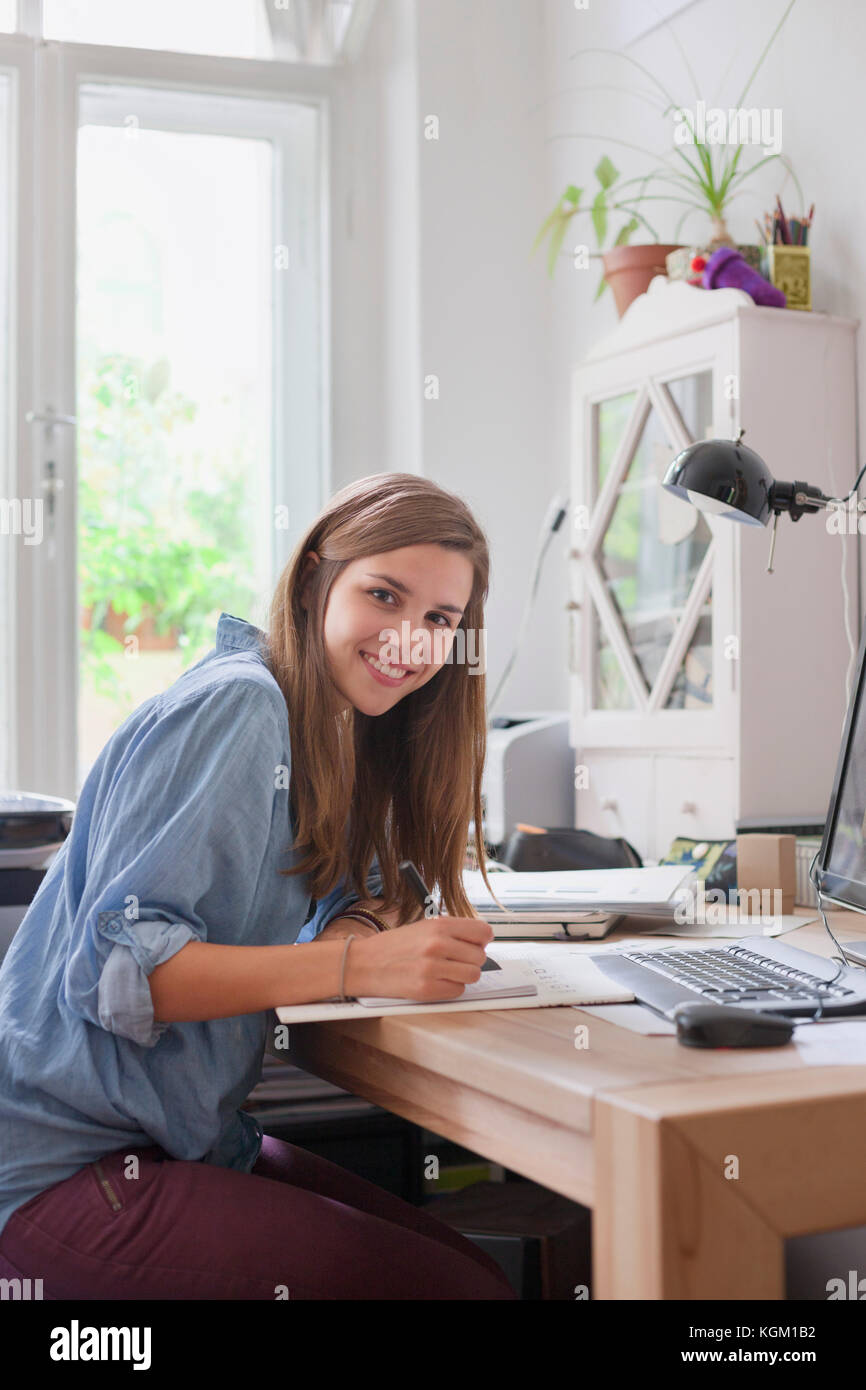 Ritratto di sorridente giovane donna iscritto al tavolo per computer in camera Foto Stock