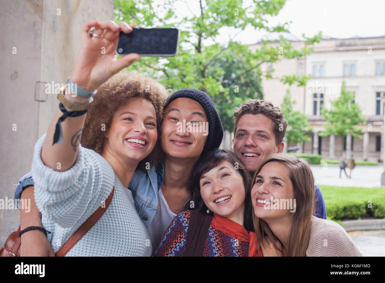 Sorridente giovane donna prendendo selfie con multi-etnico amici, Berlino, Germania Foto Stock