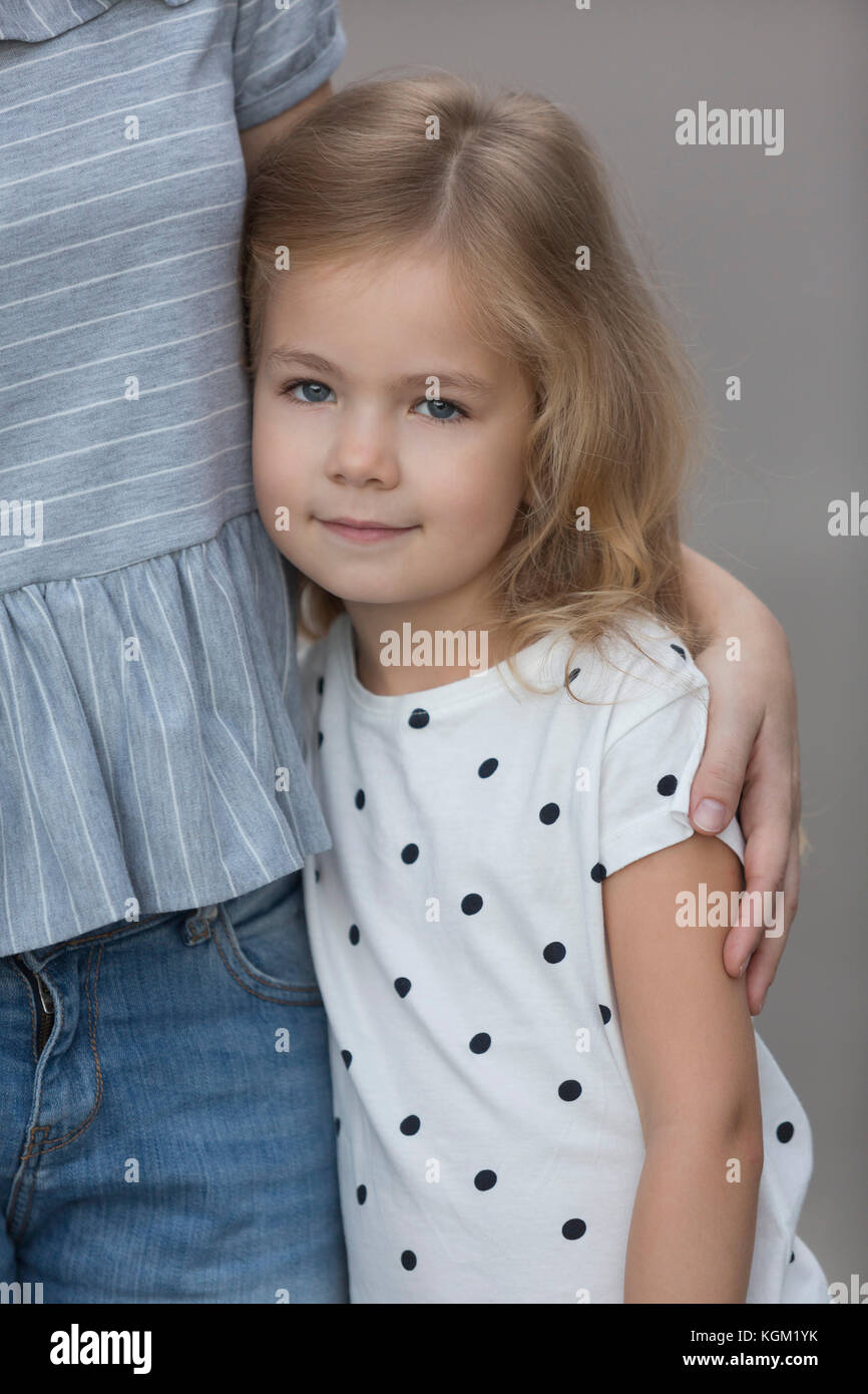 Ritratto di ragazza carina in piedi dalla madre contro lo sfondo grigio Foto Stock