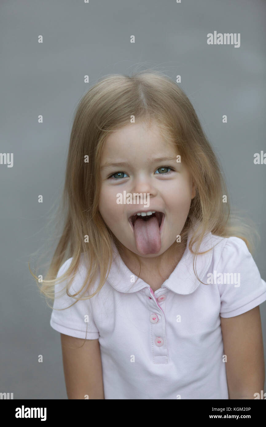 Ritratto di Allegro ragazza spuntavano lingua contro uno sfondo grigio Foto Stock