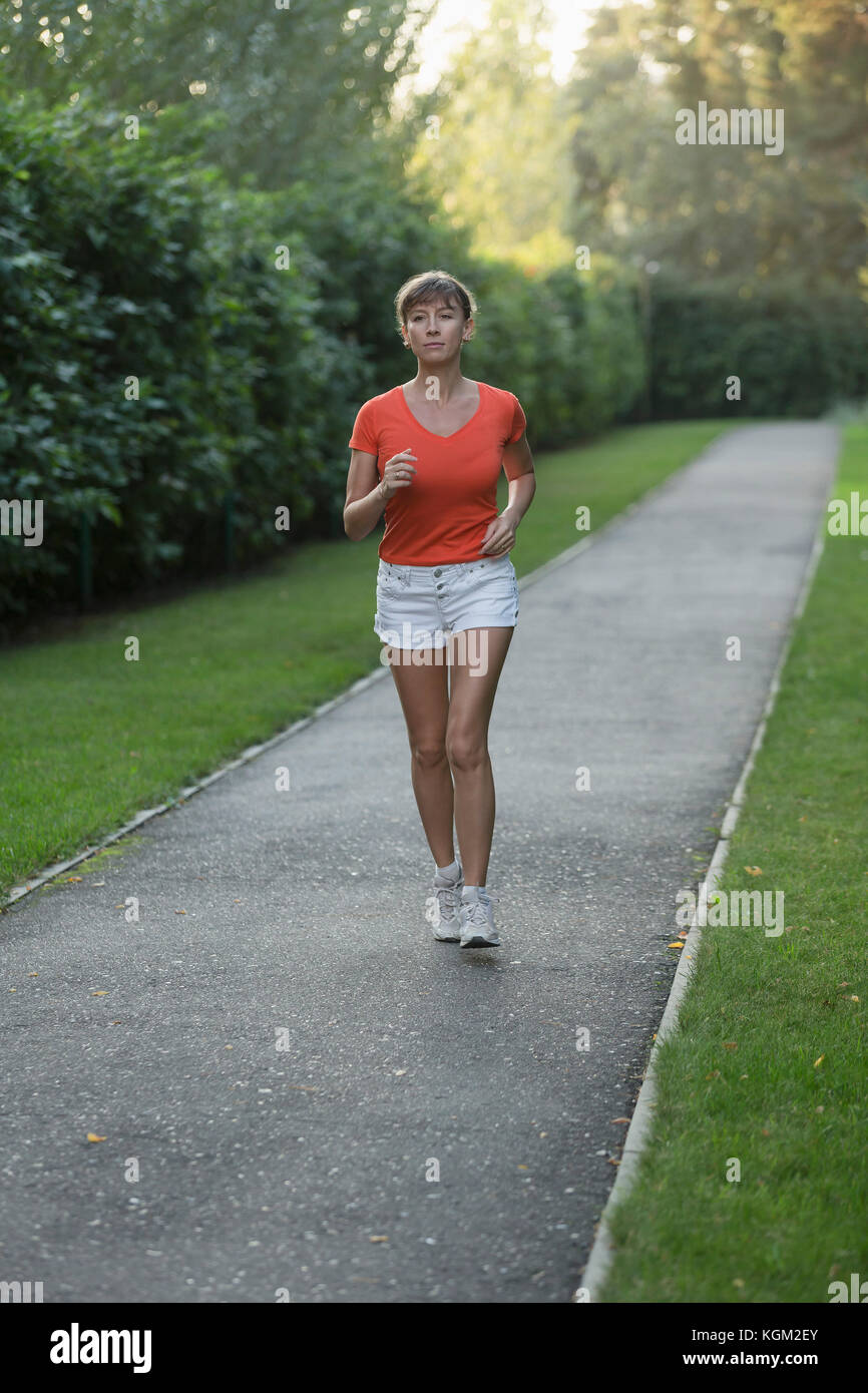 Per tutta la lunghezza della donna jogging sulla strada dalle piante Foto Stock