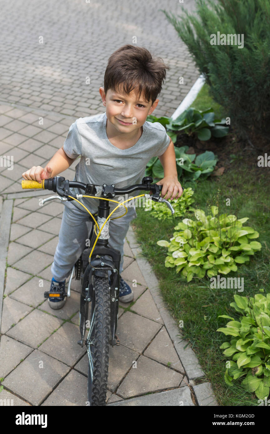 Angolo alto ritratto di ragazzo Bicicletta Equitazione su strada dalle piante Foto Stock