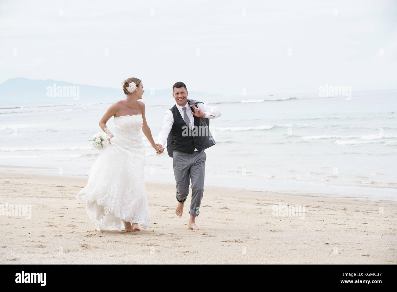 Allegro appena una coppia sposata in esecuzione su di una spiaggia di sabbia Foto Stock