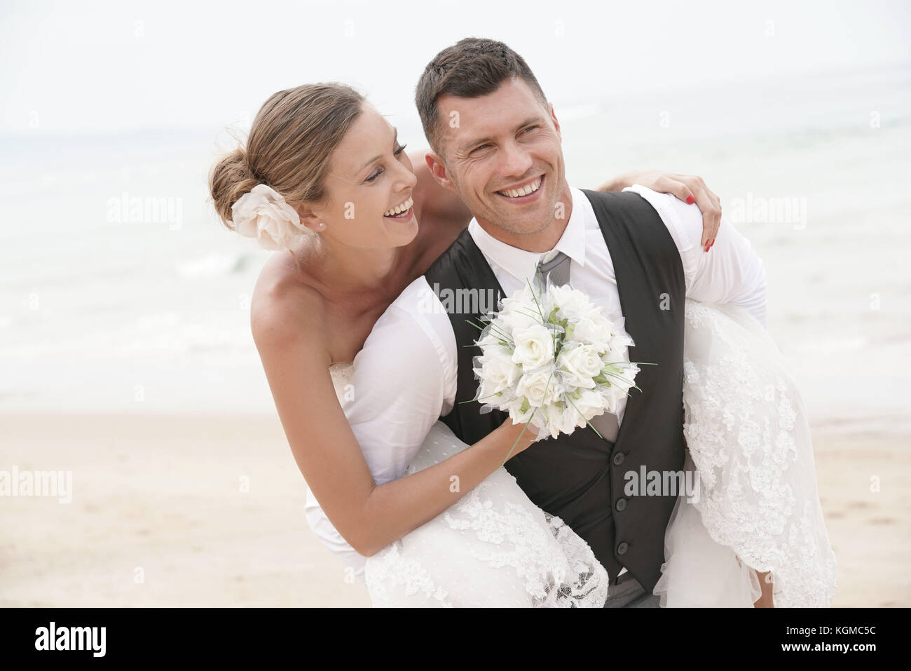 Lo sposo dando piggyback ride alla sposa sulla spiaggia Foto Stock