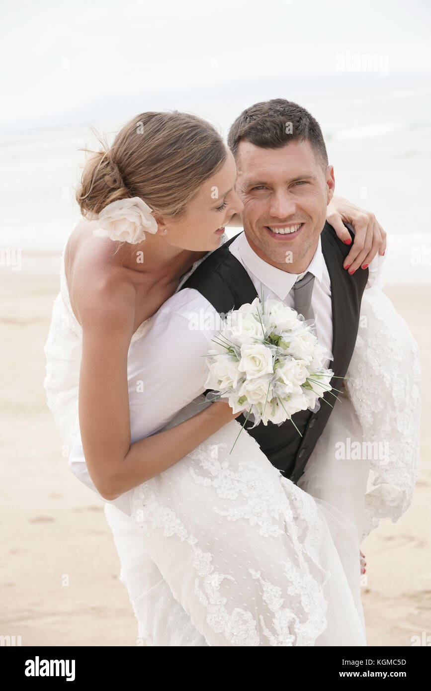 Lo sposo dando piggyback ride alla sposa sulla spiaggia Foto Stock