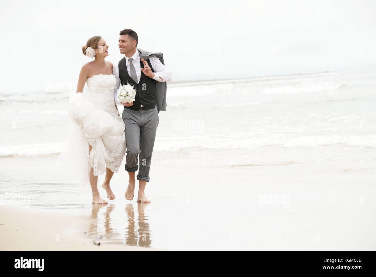 Felice sposa e lo sposo correre a piedi nudi sulla spiaggia in riva al mare Foto Stock