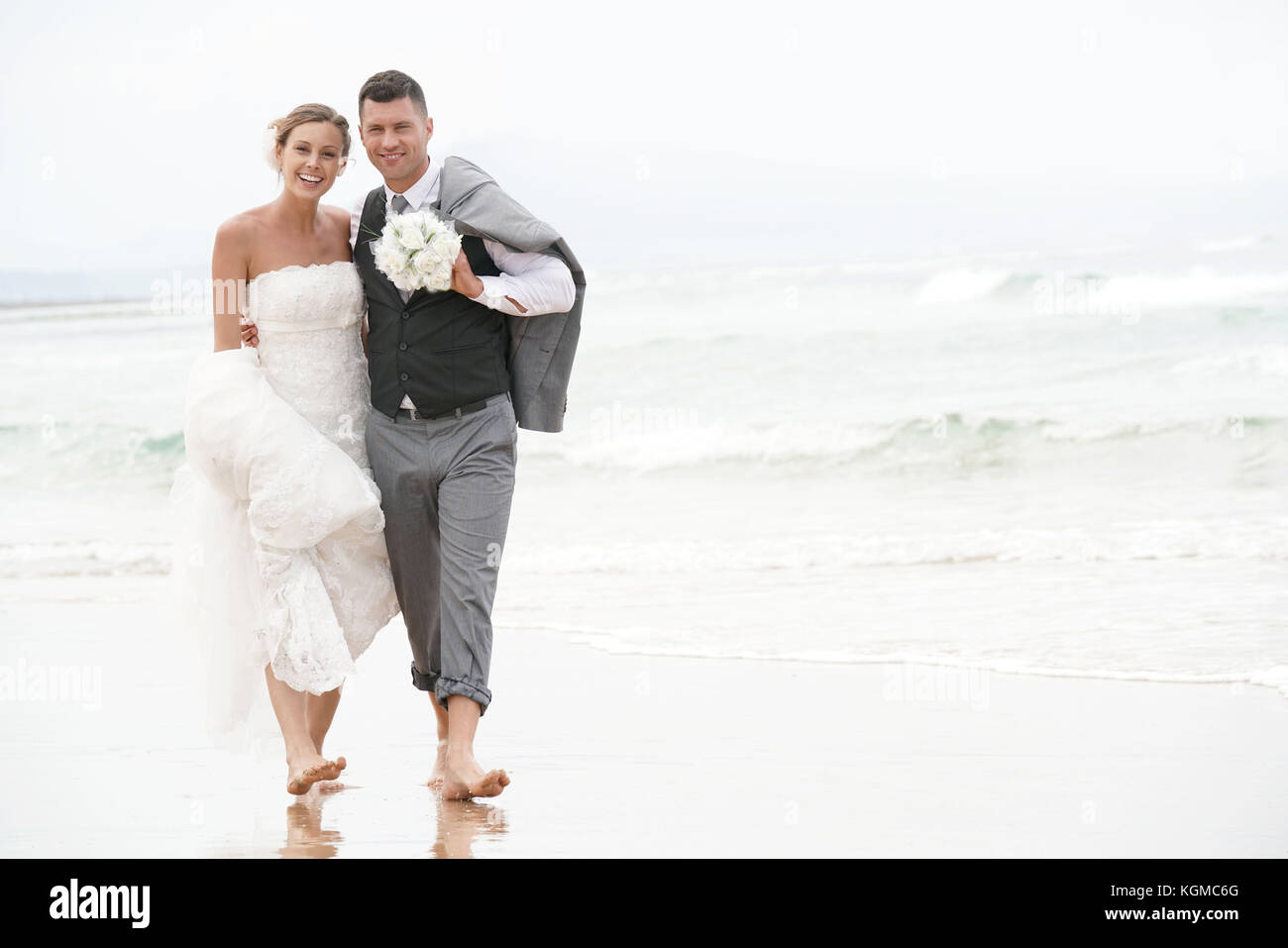 Felice sposa e lo sposo correre a piedi nudi sulla spiaggia in riva al mare Foto Stock