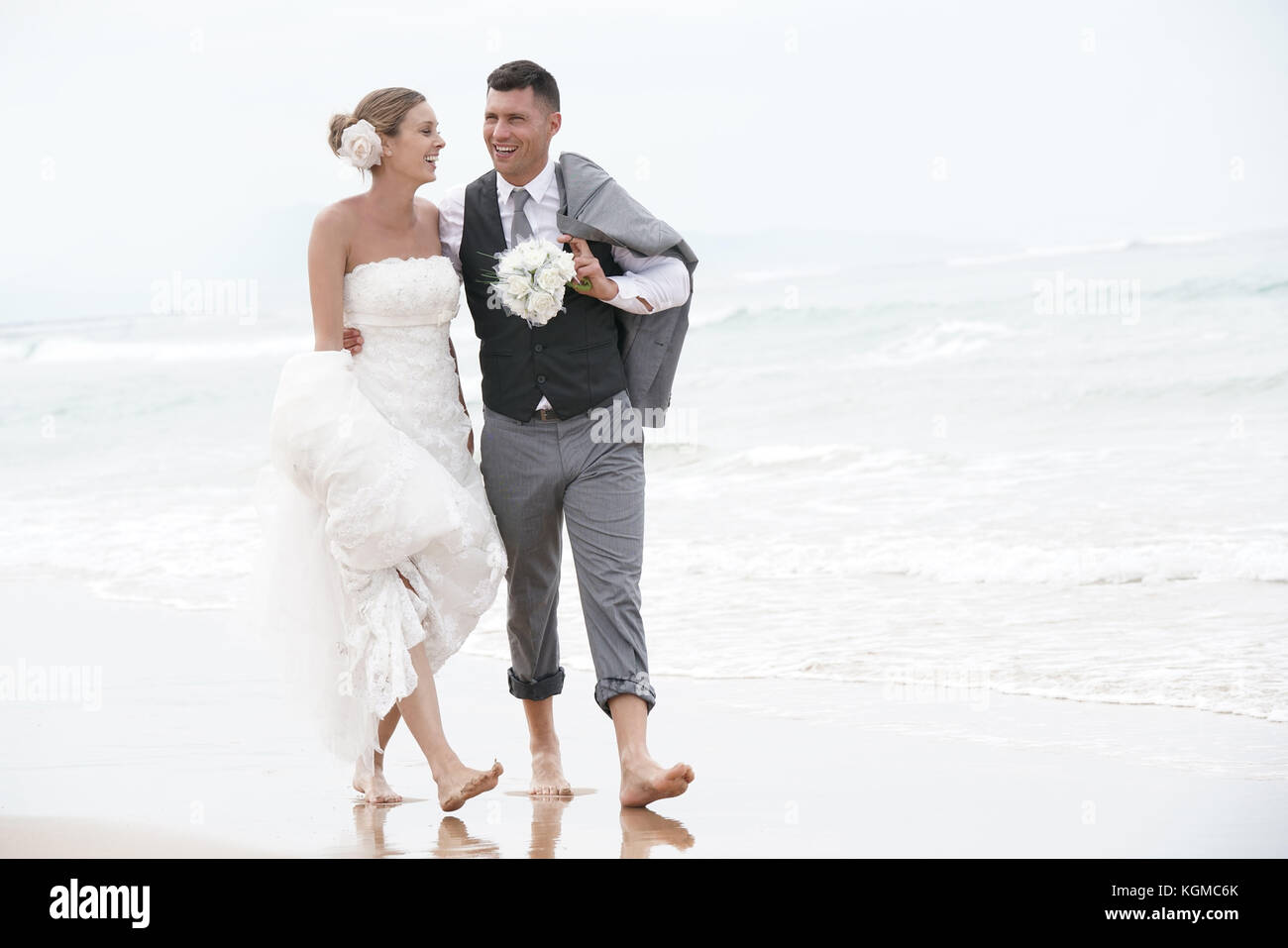 Felice sposa e lo sposo correre a piedi nudi sulla spiaggia in riva al mare Foto Stock