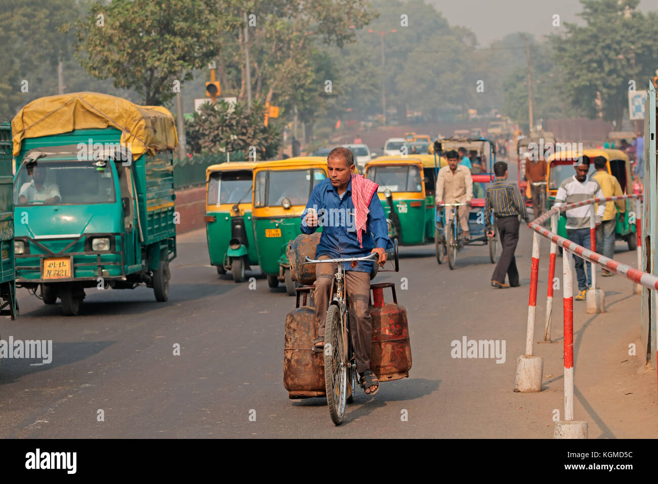 Delhi, India - 20 novembre 2015: uomo su una bicicletta nel traffico affollato con colorati di tuk-tuk veicoli e smog visibile dell'inquinamento atmosferico Foto Stock