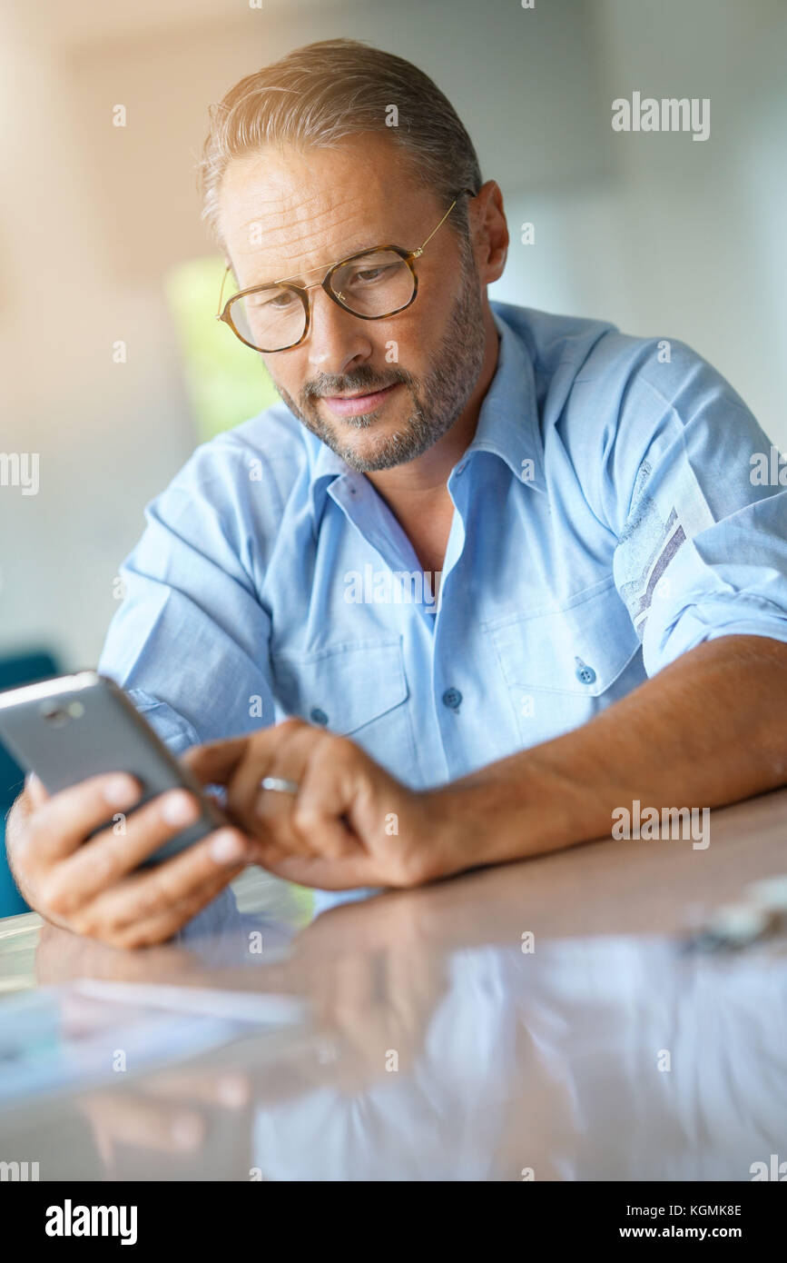 Uomo maturo con occhiali digitando messaggio sullo smartphone Foto Stock