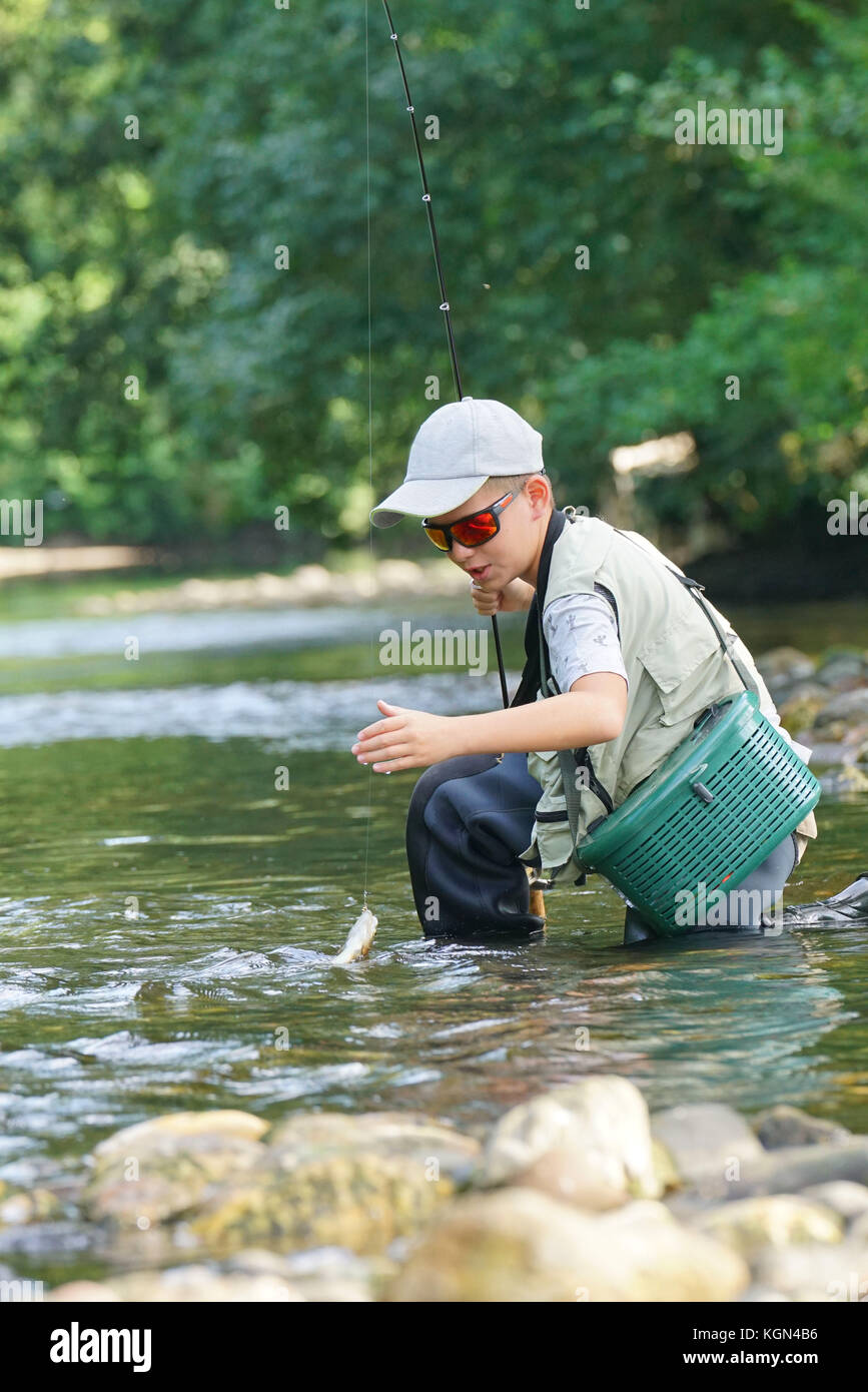 Ragazzo di cattura della trota arcobaleno nel fiume Foto Stock