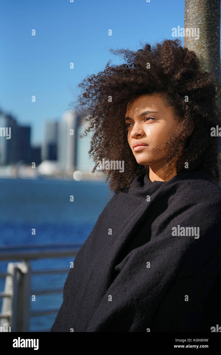 Razza mista donna in piedi dall'East River, Manhattan in background Foto Stock