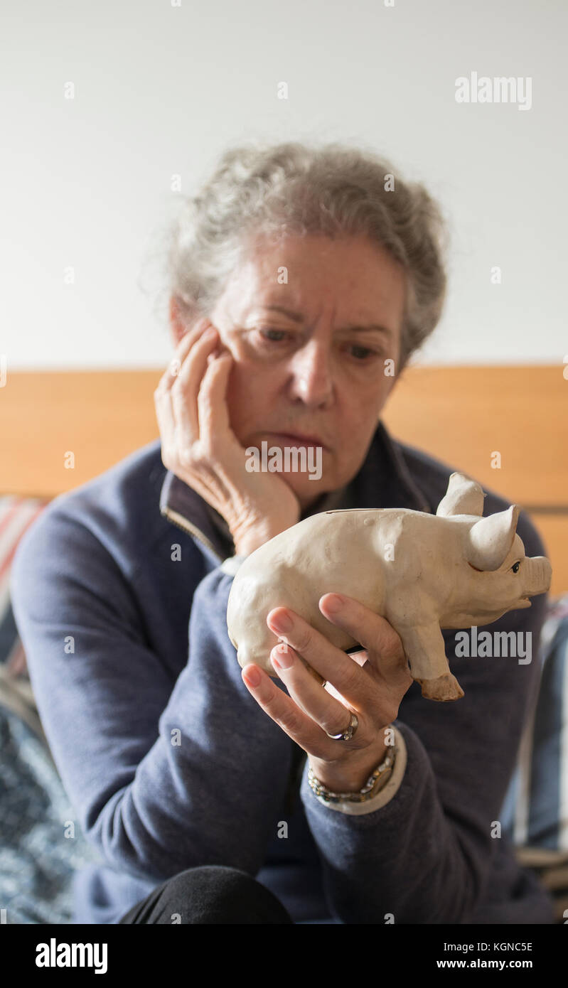 Donna anziana saver con denaro salvadanaio, cercando premuto, con la testa appoggiata sulla mano, conto di risparmio tassi di interesse rimanere tutto il tempo basso, 2017. Foto Stock