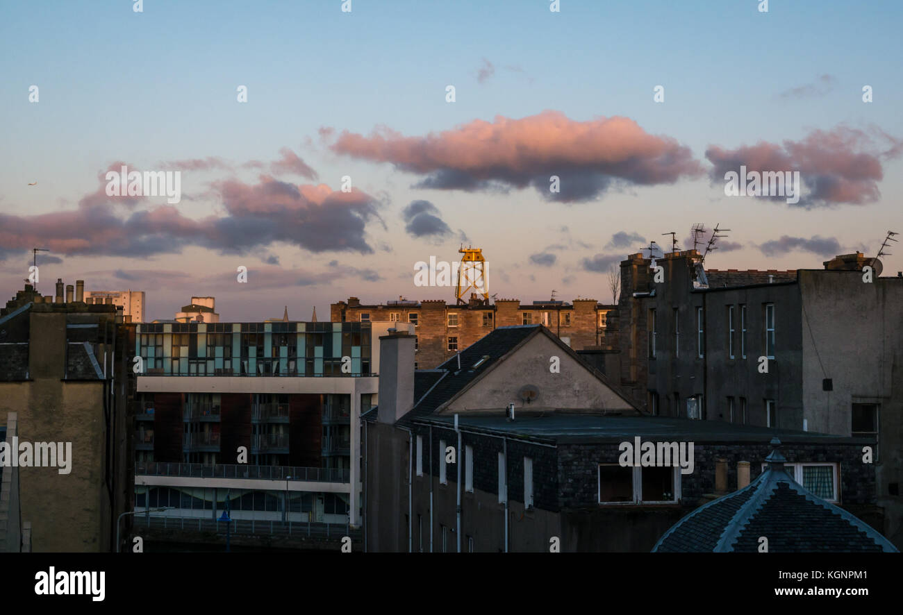 Leith, Edimburgo, Scozia, Regno Unito. Alba sopra i tetti di Leith sulla riva con nuvole rosa. Un enorme giallo turbina eolica piattaforma, una camicia di centrali eoliche in Leith Harbour towers sui tetti Foto Stock