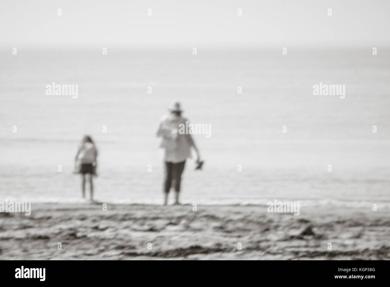 Immagine defocused della madre e della figlia al bordo dell'acqua della spiaggia di Cornish. Per le vacanze al mare dei bambini, per le passeggiate in mare, per i bambini astratto. Foto Stock