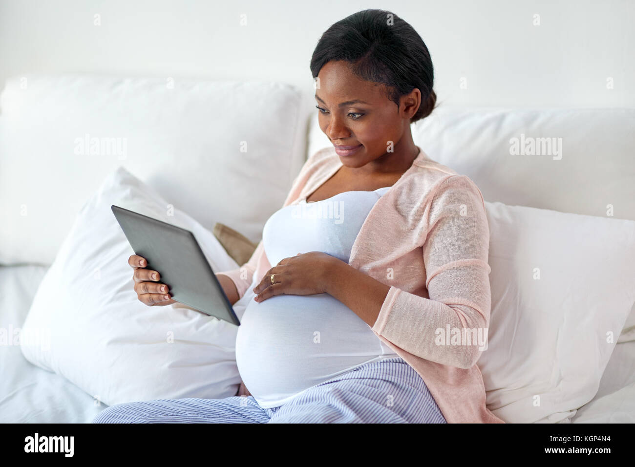 La gravidanza, tecnologia, persone e aspettativa concetto - happy africana incinta donna americana con tablet pc computer nel letto di casa Foto Stock