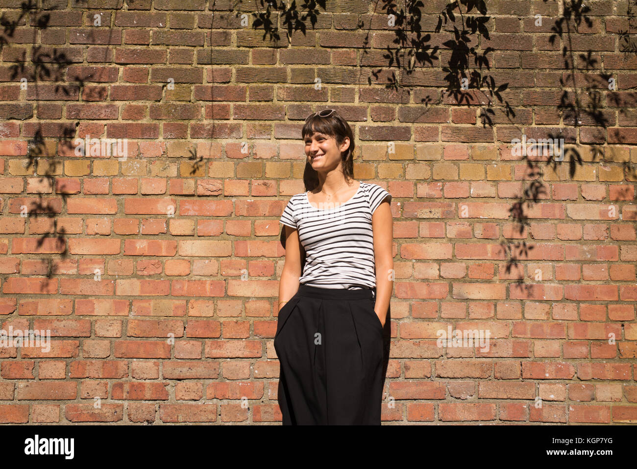 Giovane Donna vestita di urbano in stile minimale con il bianco e nero a  strisce maglietta e pantaloni neri. Un muro di mattoni come sfondo Foto  stock - Alamy