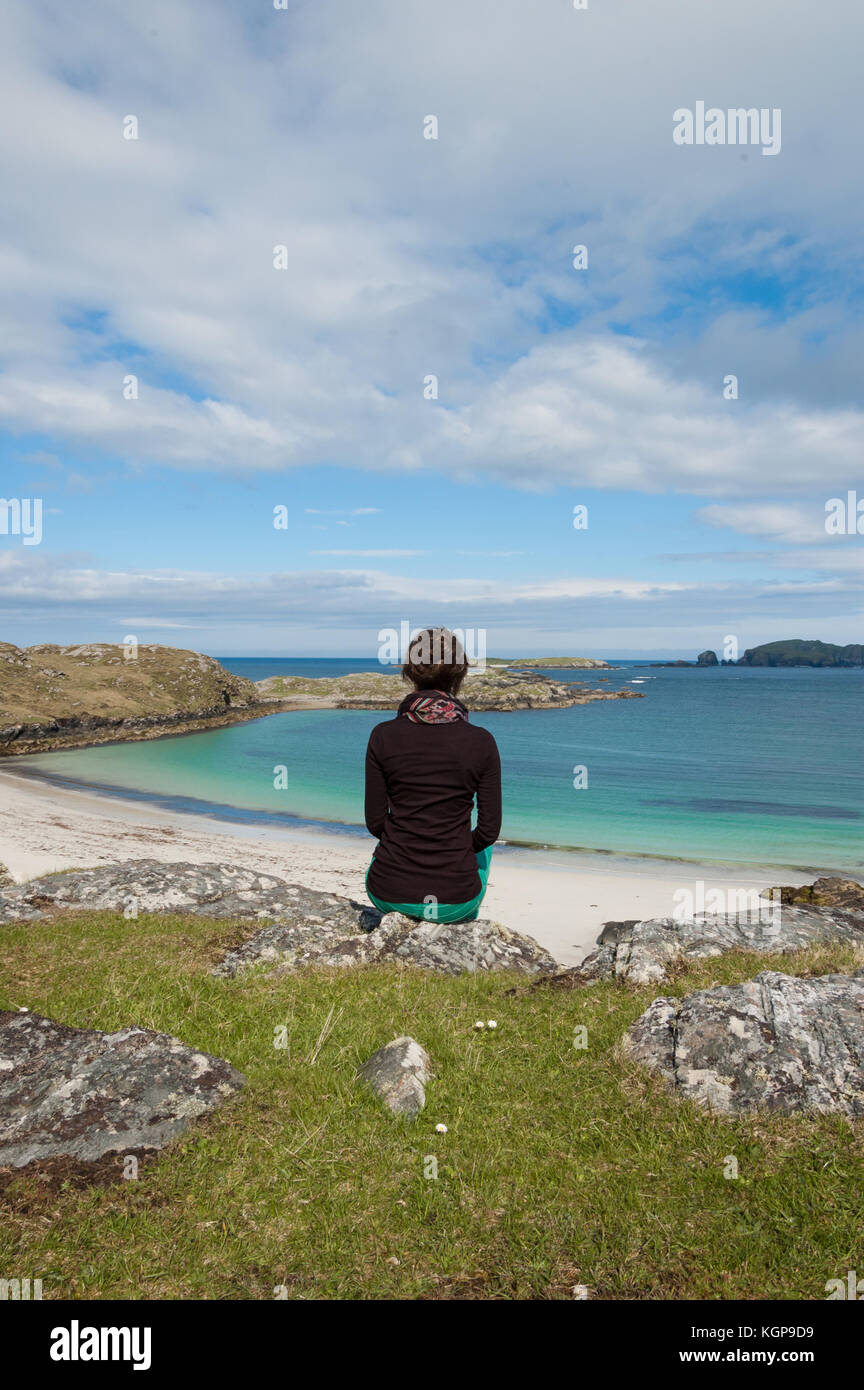 Giovane donna turista seduto davanti a un deserto spiaggia bianca con mare azzurro dell'isola di Lewis, Ebridi Esterne, Scozia (UK) Foto Stock