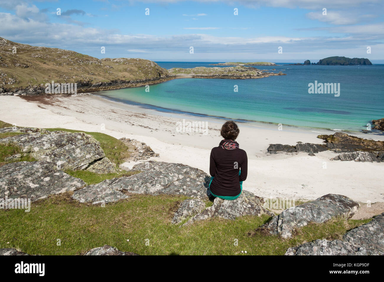 Giovane donna turista seduto davanti a un deserto spiaggia bianca con mare azzurro dell'isola di Lewis, Ebridi Esterne, Scozia (UK) Foto Stock