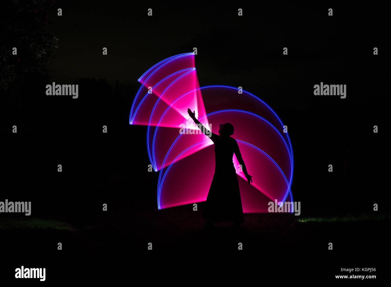 Silhouette di donna isolato che raggiunge il cielo circondato da volute di magica luce rosa. Oscurati scena notturna; magic effetto di luce. Foto Stock