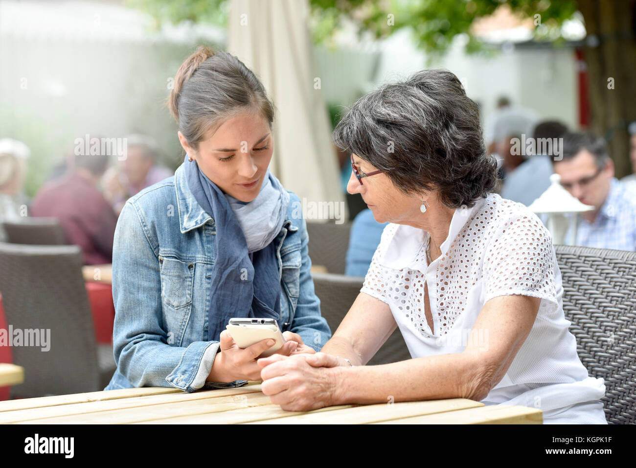 Donna anziana e accompagnatore a casa nella terrazza del caffè con smartphone Foto Stock