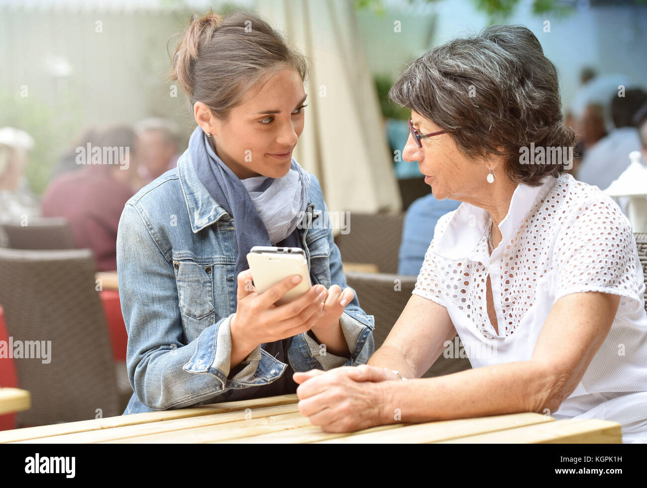 Donna anziana e accompagnatore a casa nella terrazza del caffè con smartphone Foto Stock