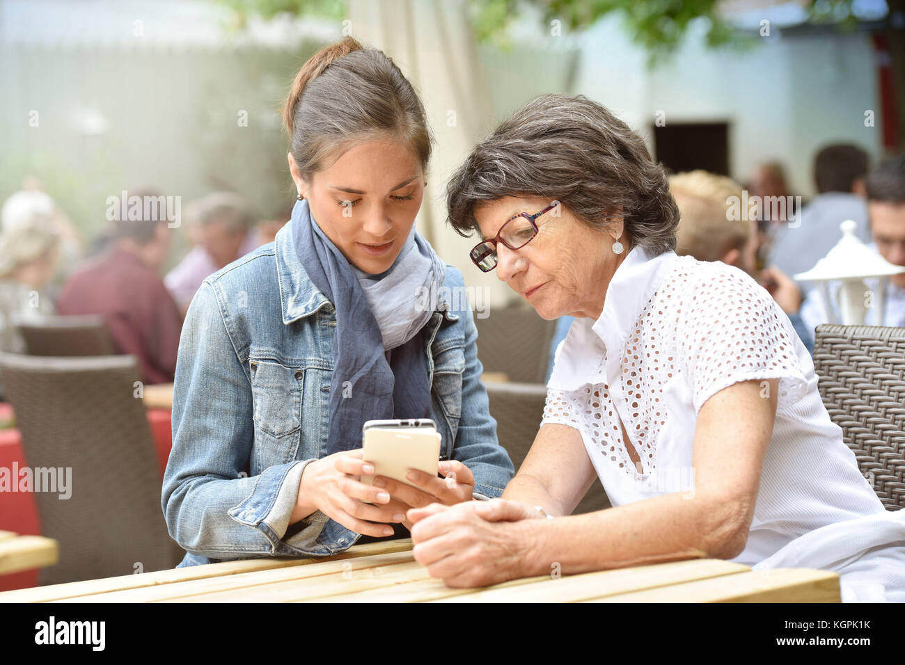 Donna anziana e accompagnatore a casa nella terrazza del caffè con smartphone Foto Stock