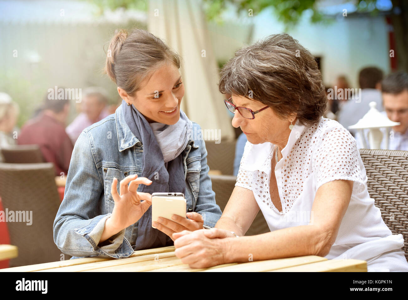 Donna anziana e accompagnatore a casa nella terrazza del caffè con smartphone Foto Stock