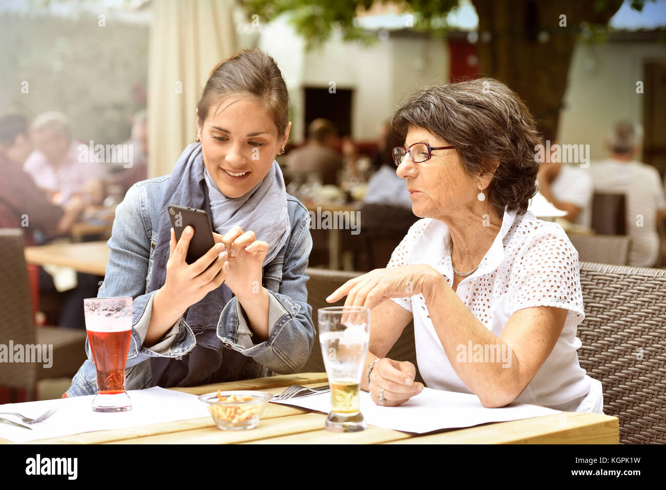 Donna anziana e accompagnatore a casa nella terrazza del caffè con smartphone Foto Stock