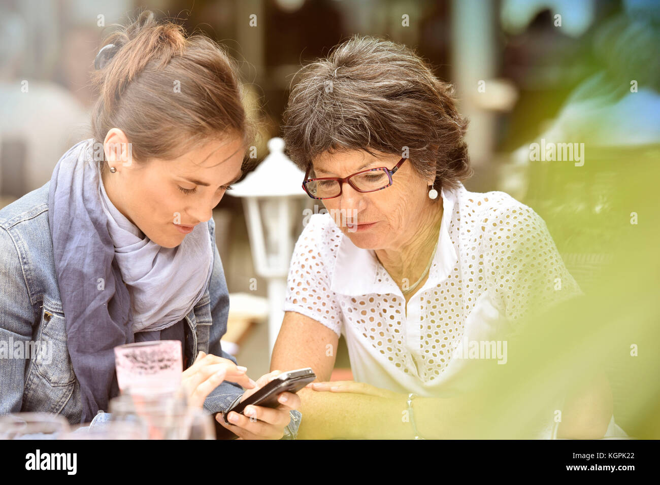Donna anziana e accompagnatore a casa nella terrazza del caffè con smartphone Foto Stock
