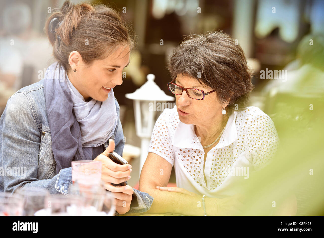 Donna anziana e accompagnatore a casa nella terrazza del caffè con smartphone Foto Stock