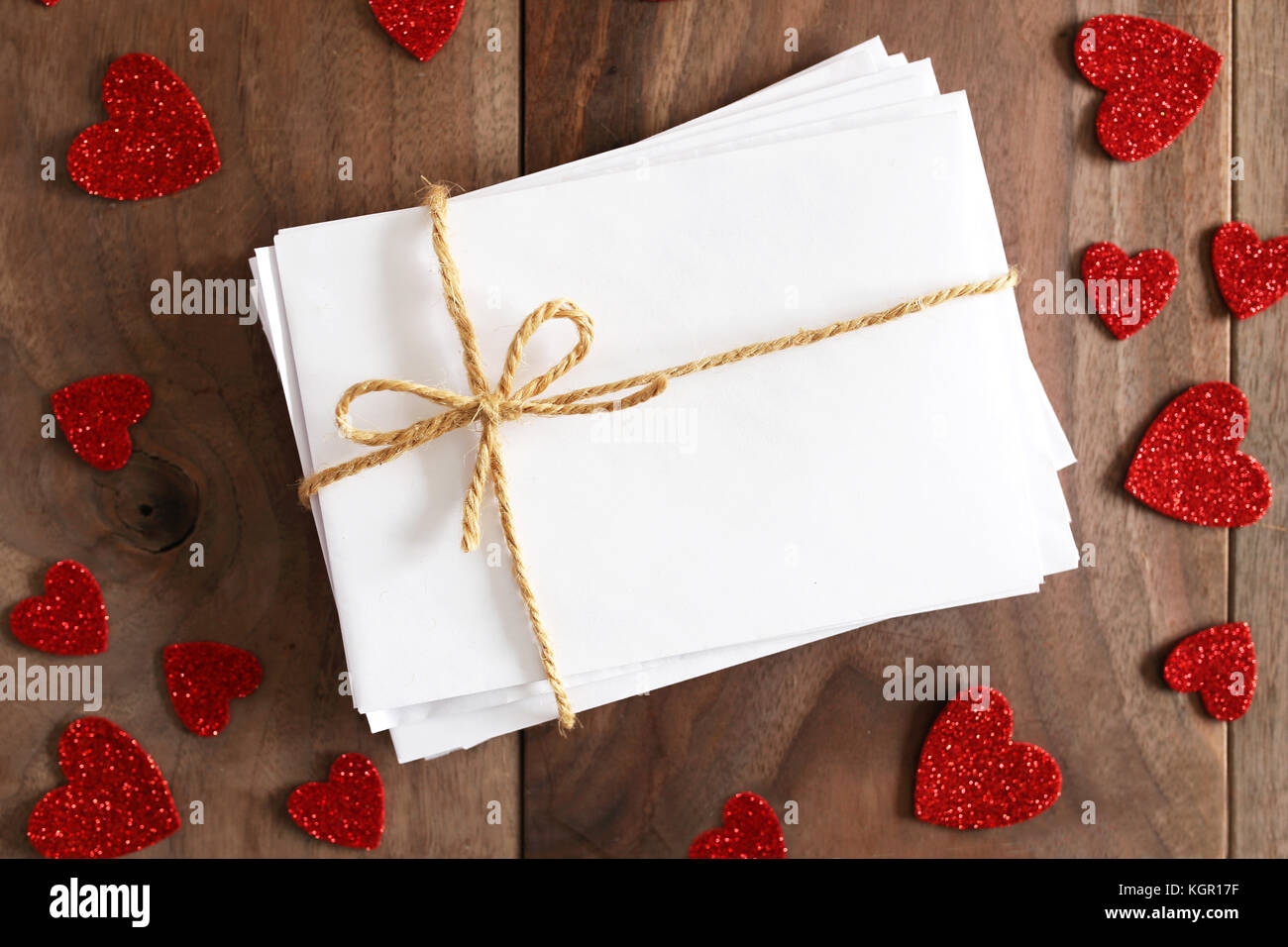 Un pacco di lettere di amore nel bianco buste bianche legata con lo spago stringa prua è seduto su un rustico di legno di ciliegio listone tabella, circondato da Valentine lui Foto Stock