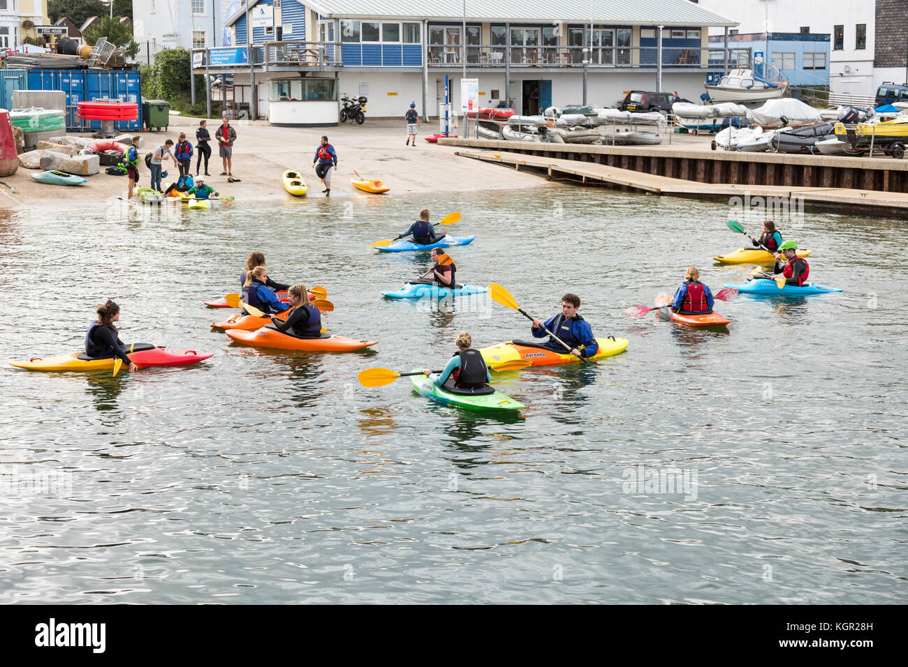 Giovani kayakers formazione in Falmouth Harbour, UK con quayside e barche in background. Foto Stock