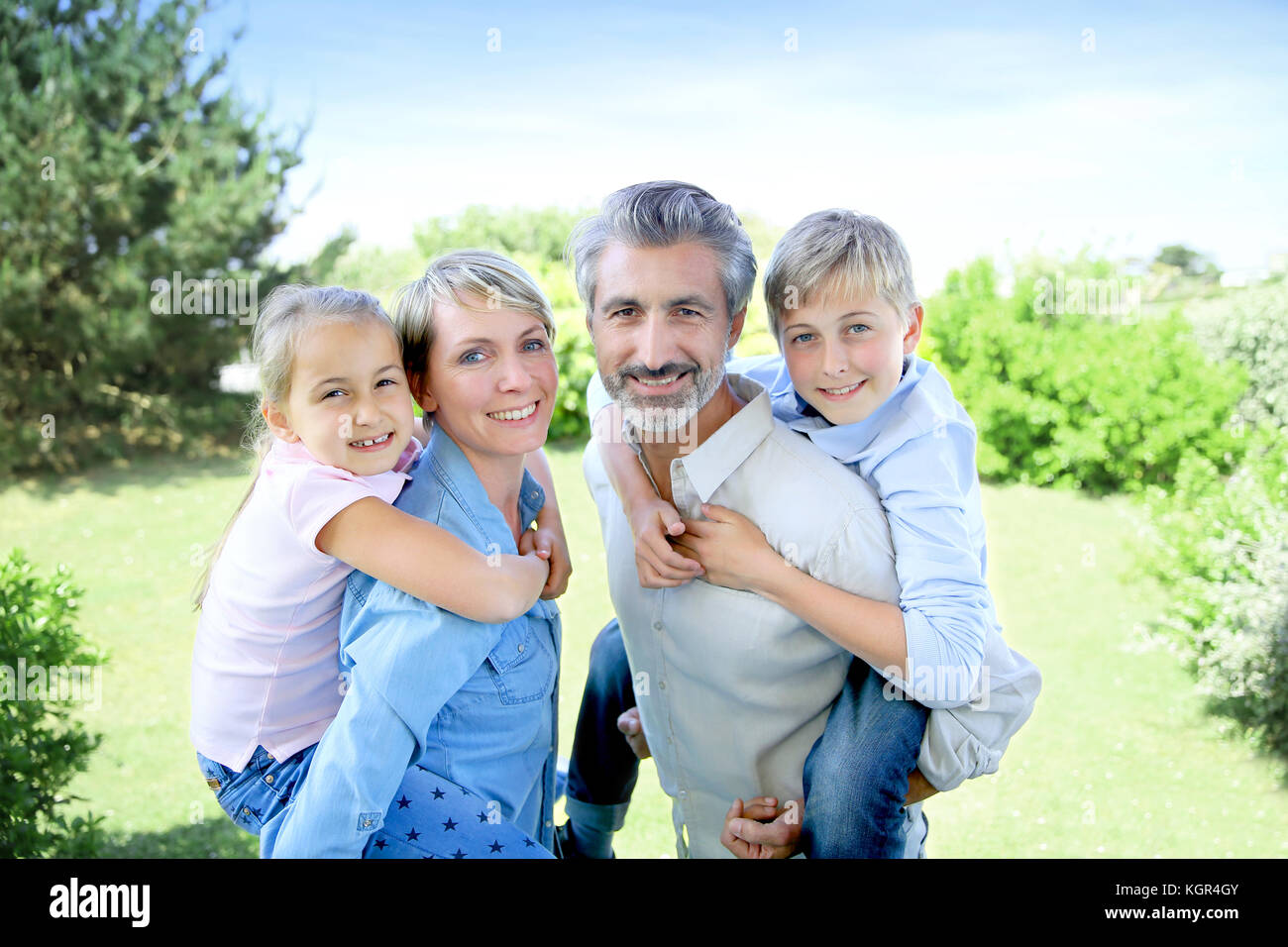 I genitori dando piggyback ride per i bambini in giardino Foto Stock