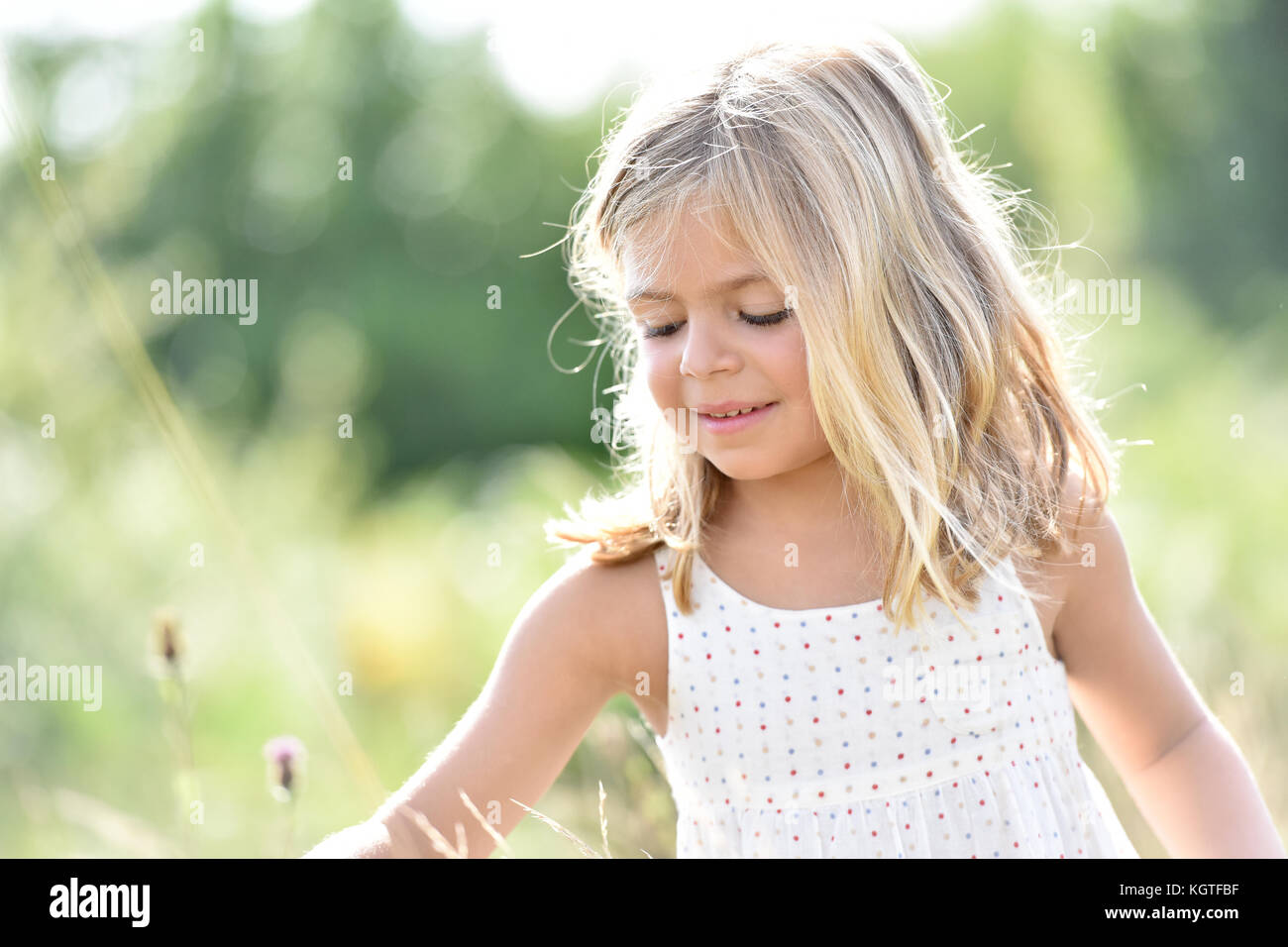 Ritratto di incantevole piccola ragazza bionda a caccia di fiori nel campo Foto Stock